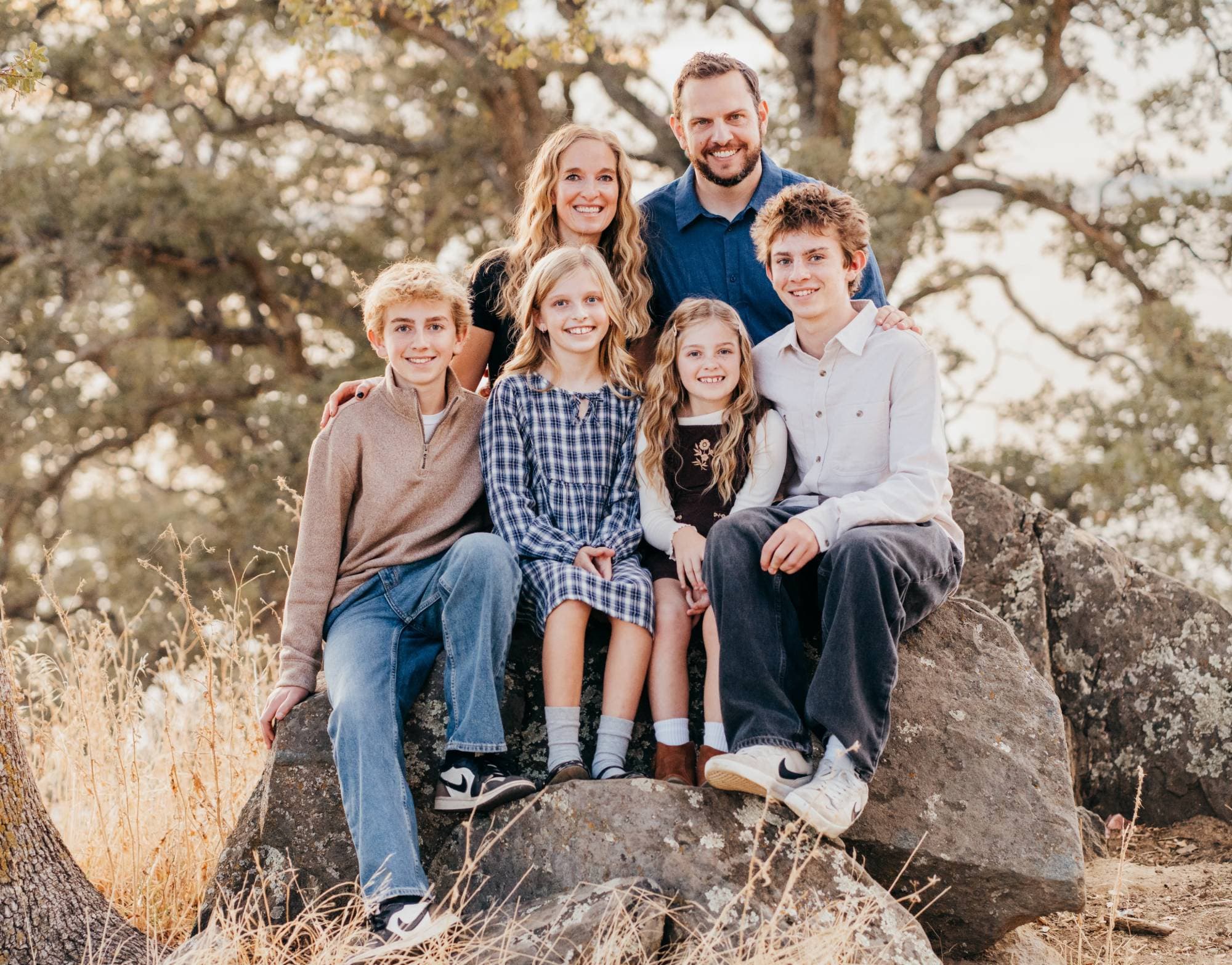 Family of six poses together on a boulder, parents standing behind their four children