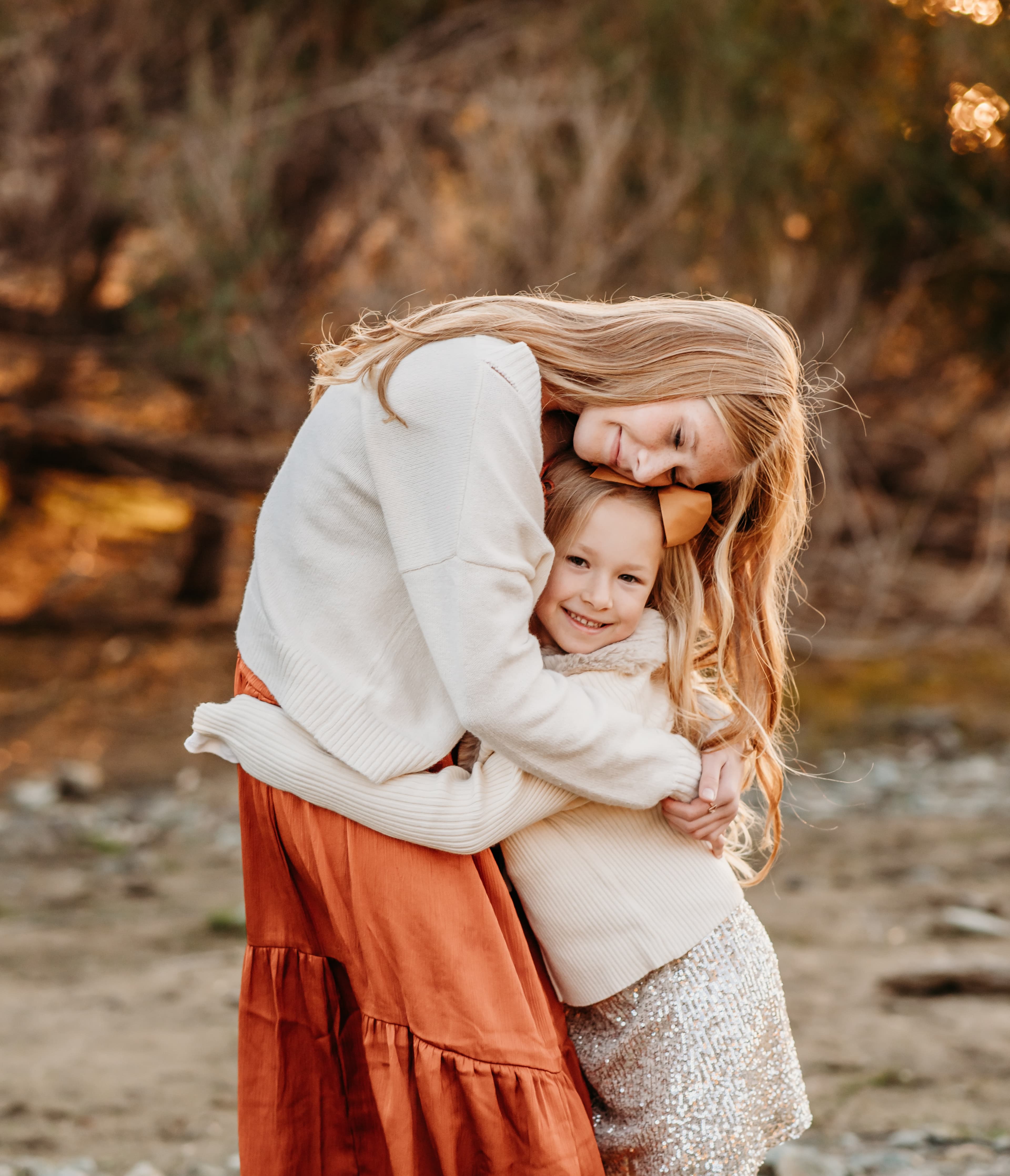 Mother embraces her young daughter cheek to cheek, warm golden bokeh light behind them