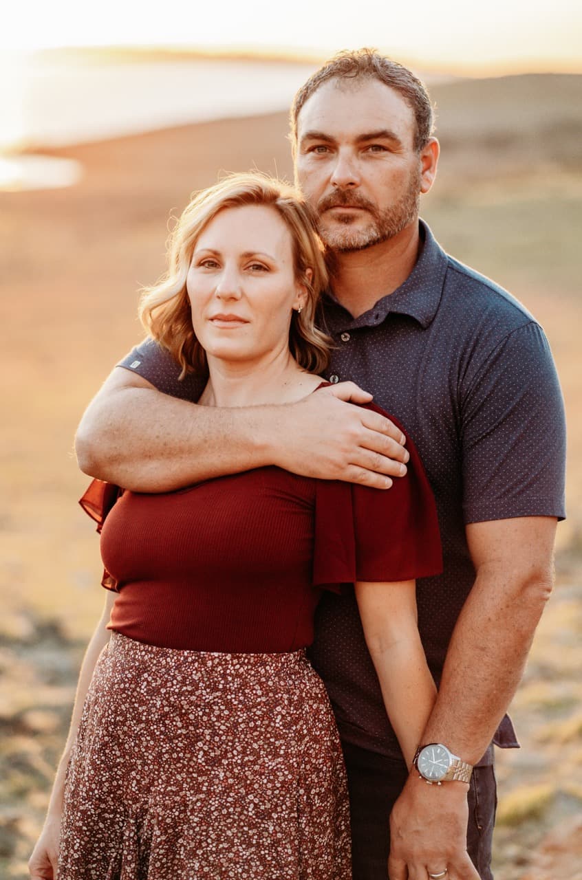 Couple embraces on a sunset beach, she in a burgundy off-shoulder top