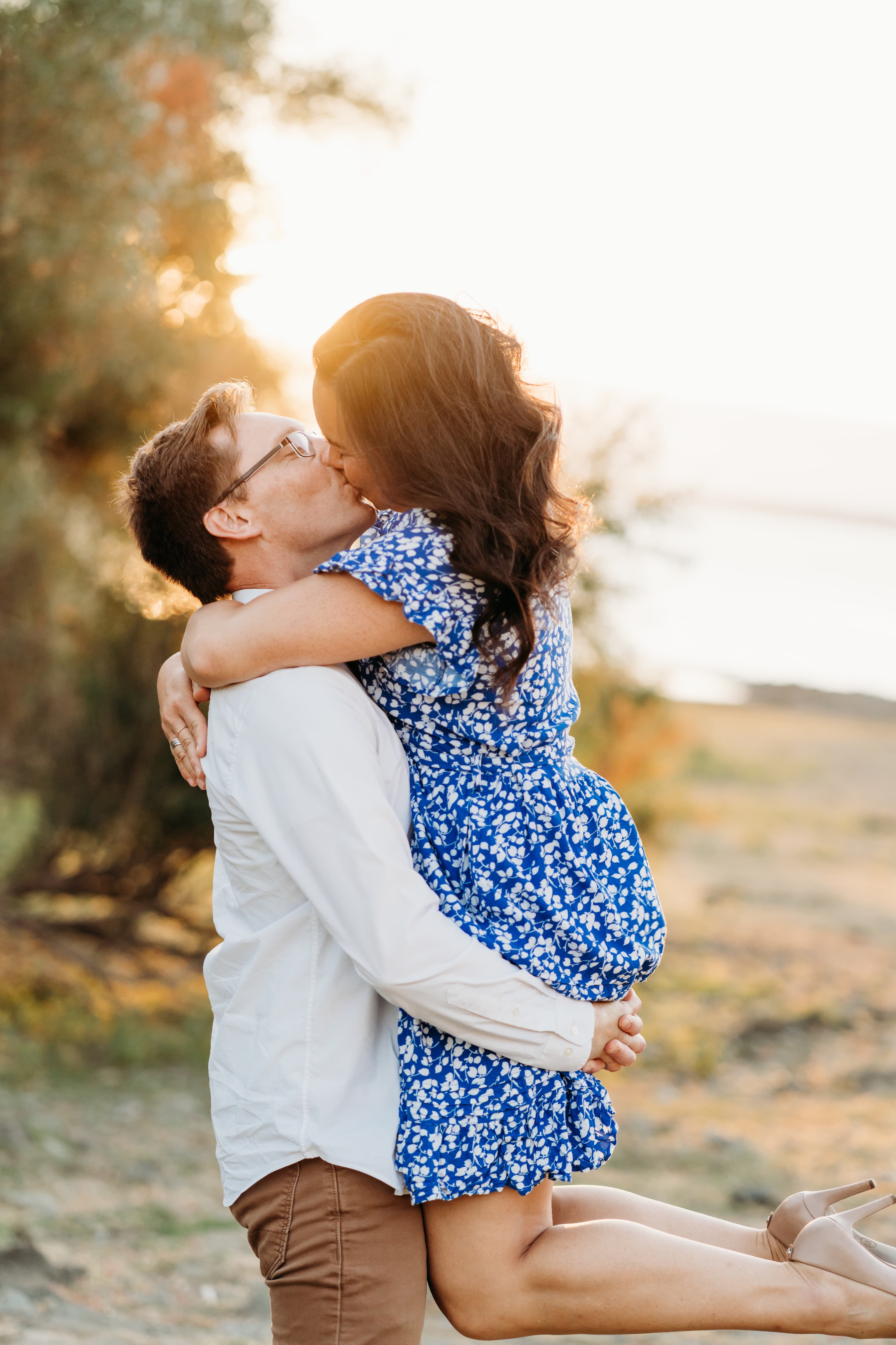 Man lifts his laughing partner off the ground for a kiss in a golden, sunlit field