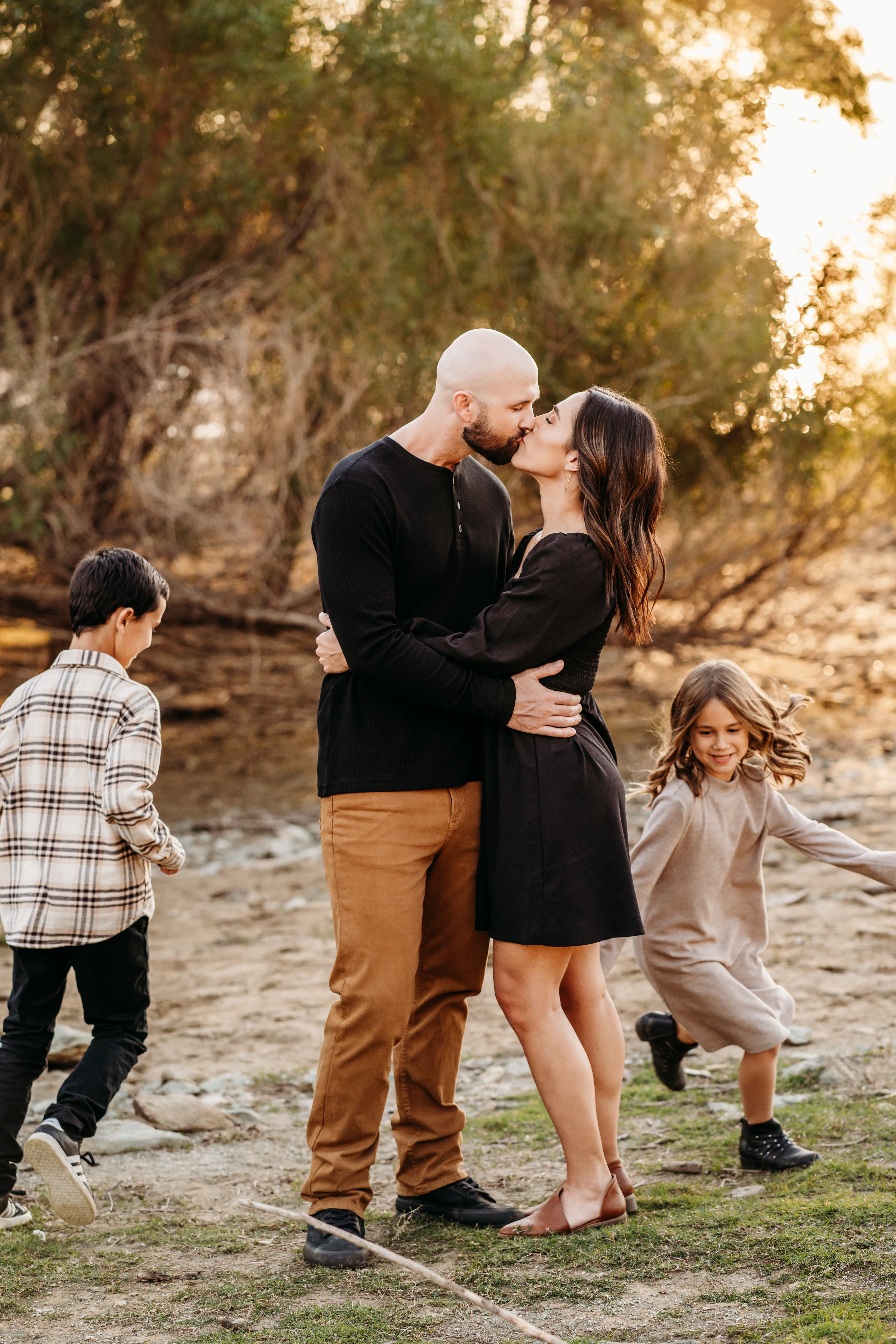 Parents share a kiss while their two children play together near a creek bed