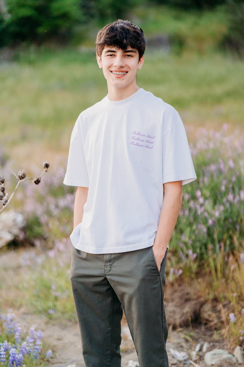 Teen boy in a white graphic tee smiling in a wildflower field