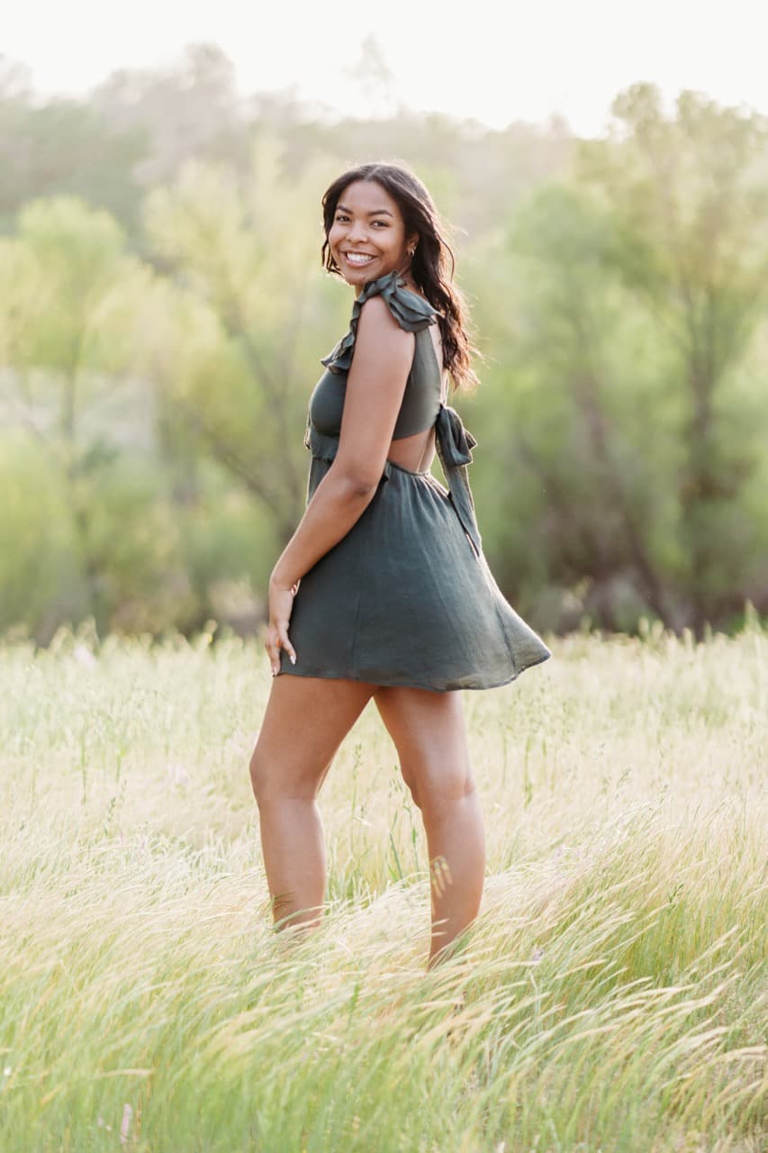 Young woman in a green ruffle dress smiling over her shoulder in a golden field