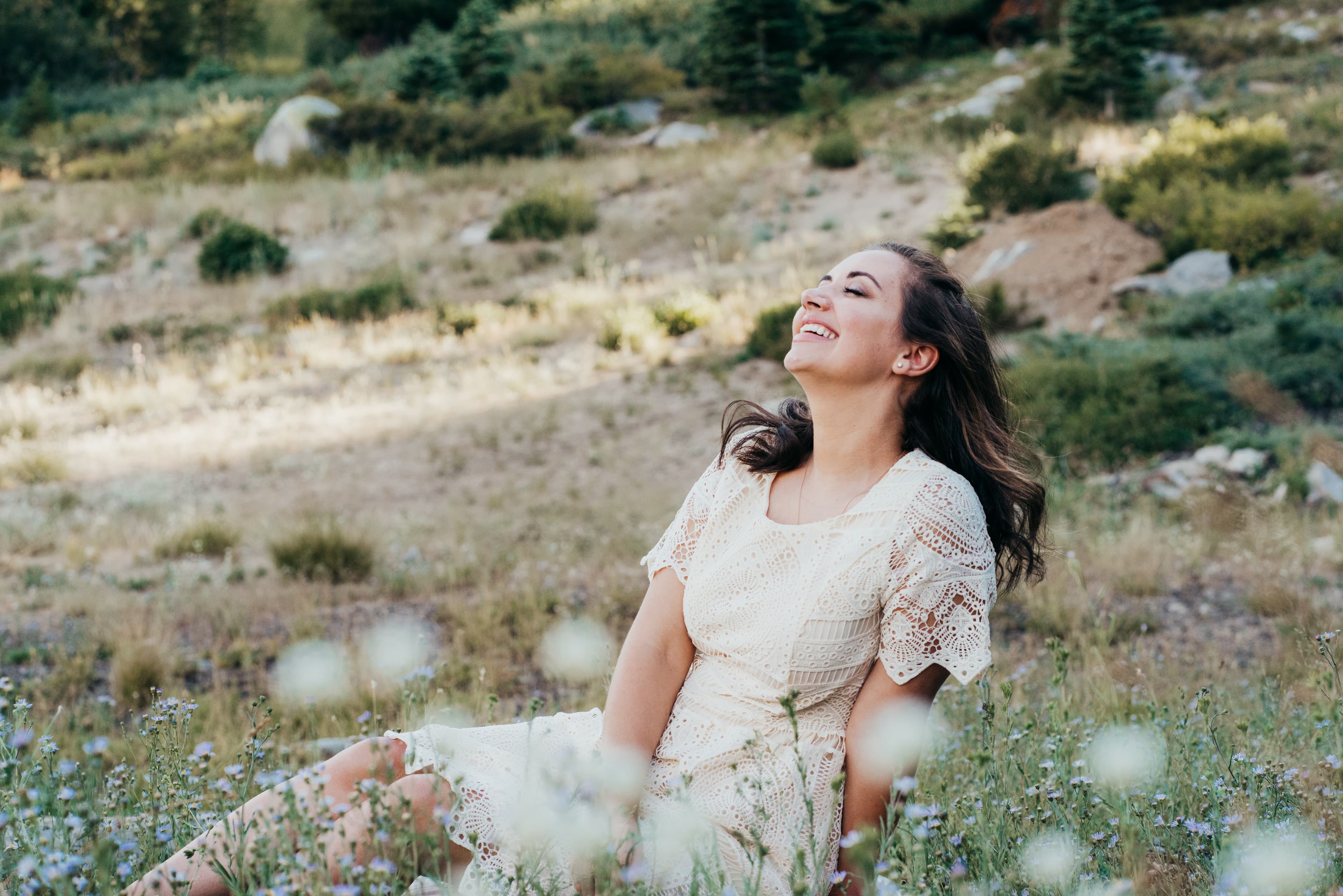 Young woman in a white lace dress laughing joyfully in a wildflower meadow