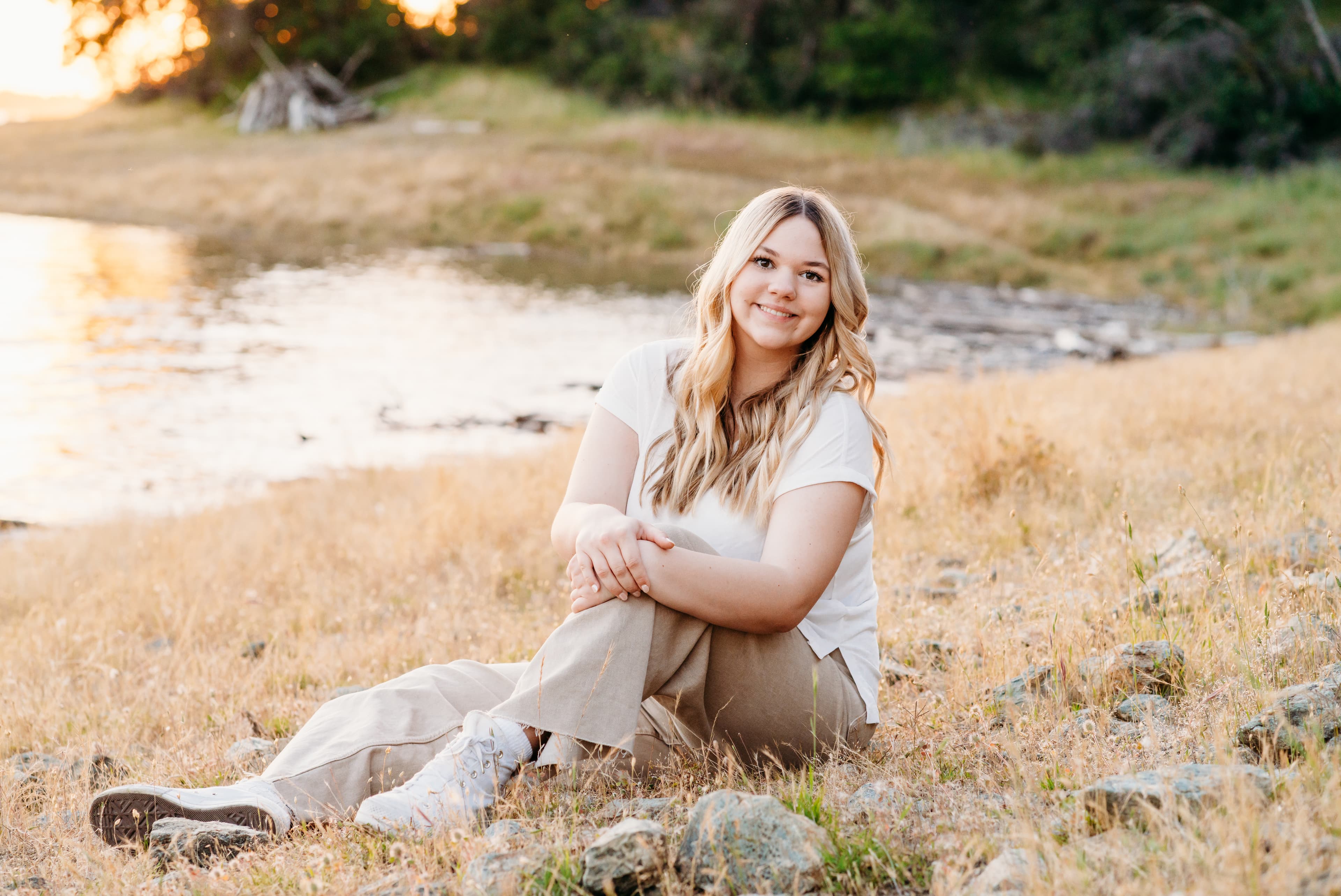 Young woman in a white tee sitting on a rocky lakeshore at sunset
