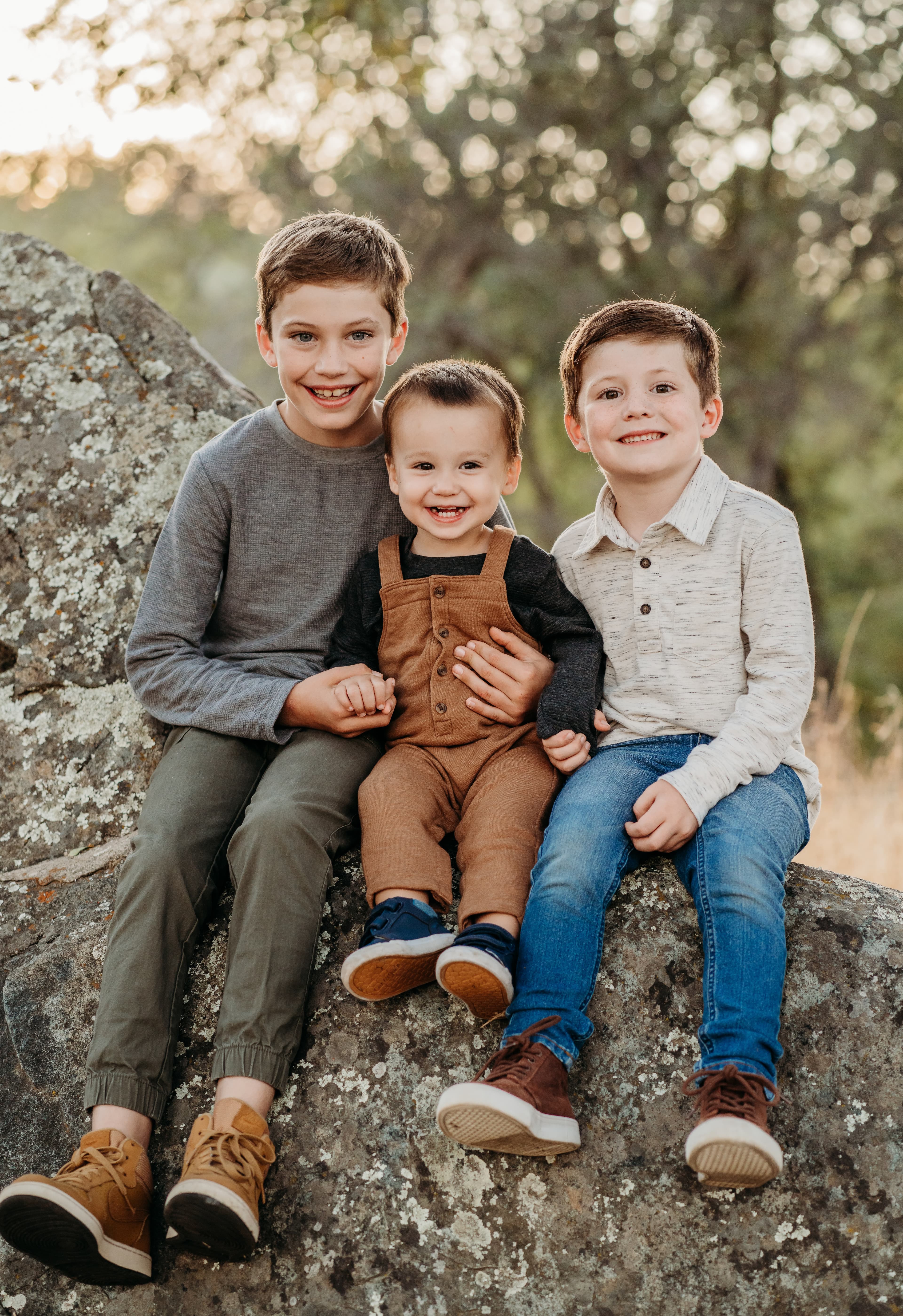 Three brothers sit together smiling on a large lichen-covered rock